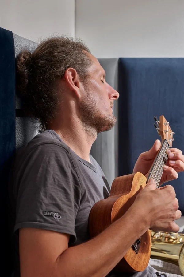 Mężczyzna gra na instrumencie i opiera się o panele tapicerowane w szarym i granatowym kolorze